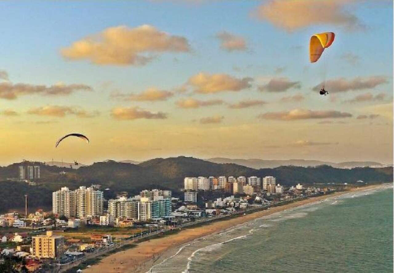 Praia Brava vista do alto ao pôr do sol, com voos de parapente