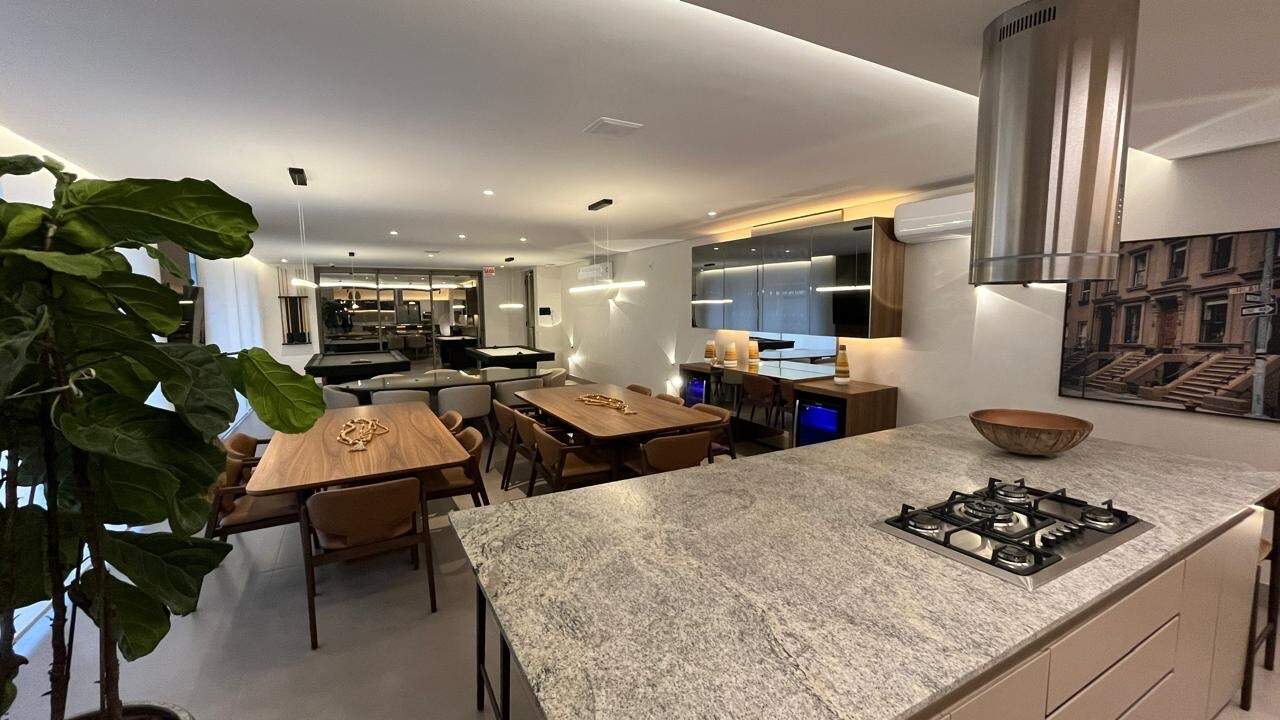 Bancada com cooktop no espaço gourmet, com as mesas e a sala de jogos ao fundo