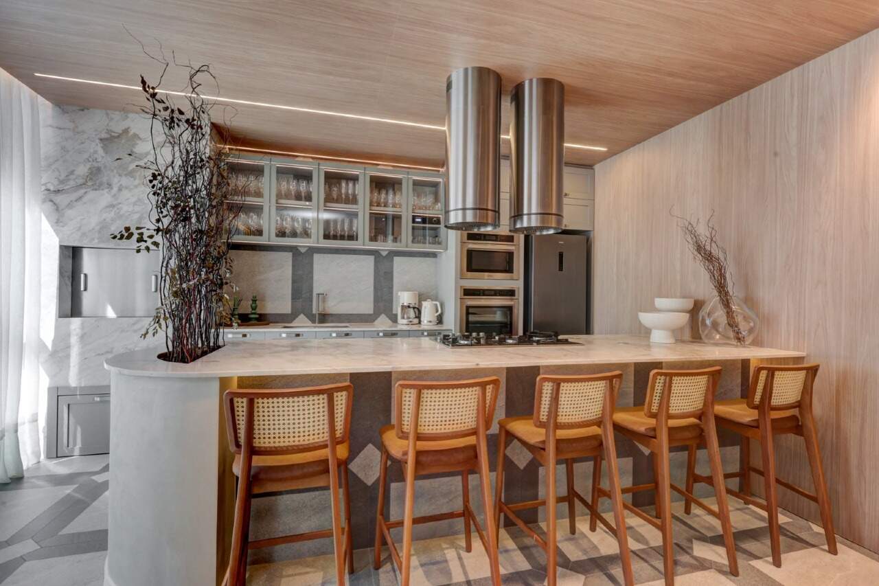 Espaço gourmet com ilha, cooktop e banquetas de madeira