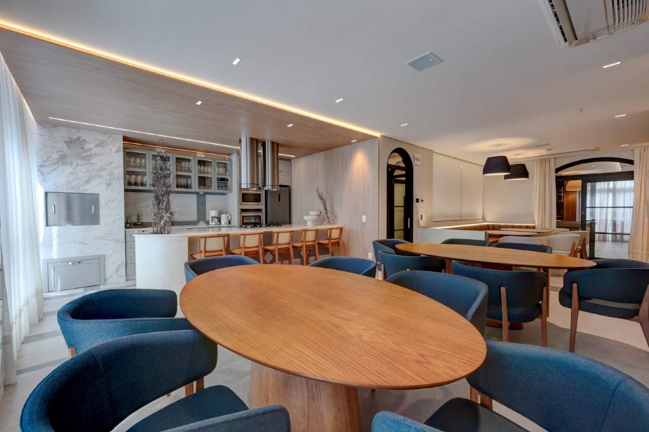 Salão de festas com mesa oval e cozinha integrada