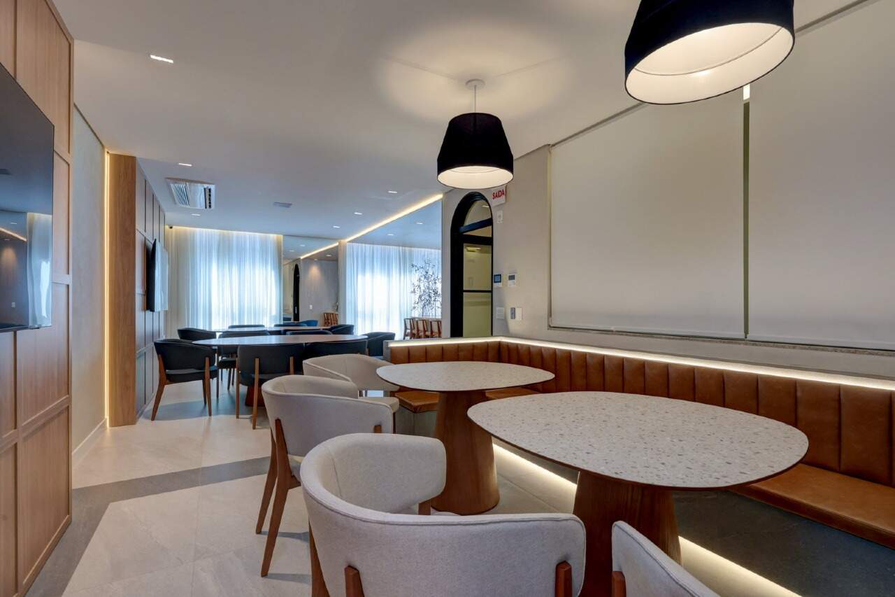 Lounge com mesas, banco estofado e iluminação indireta