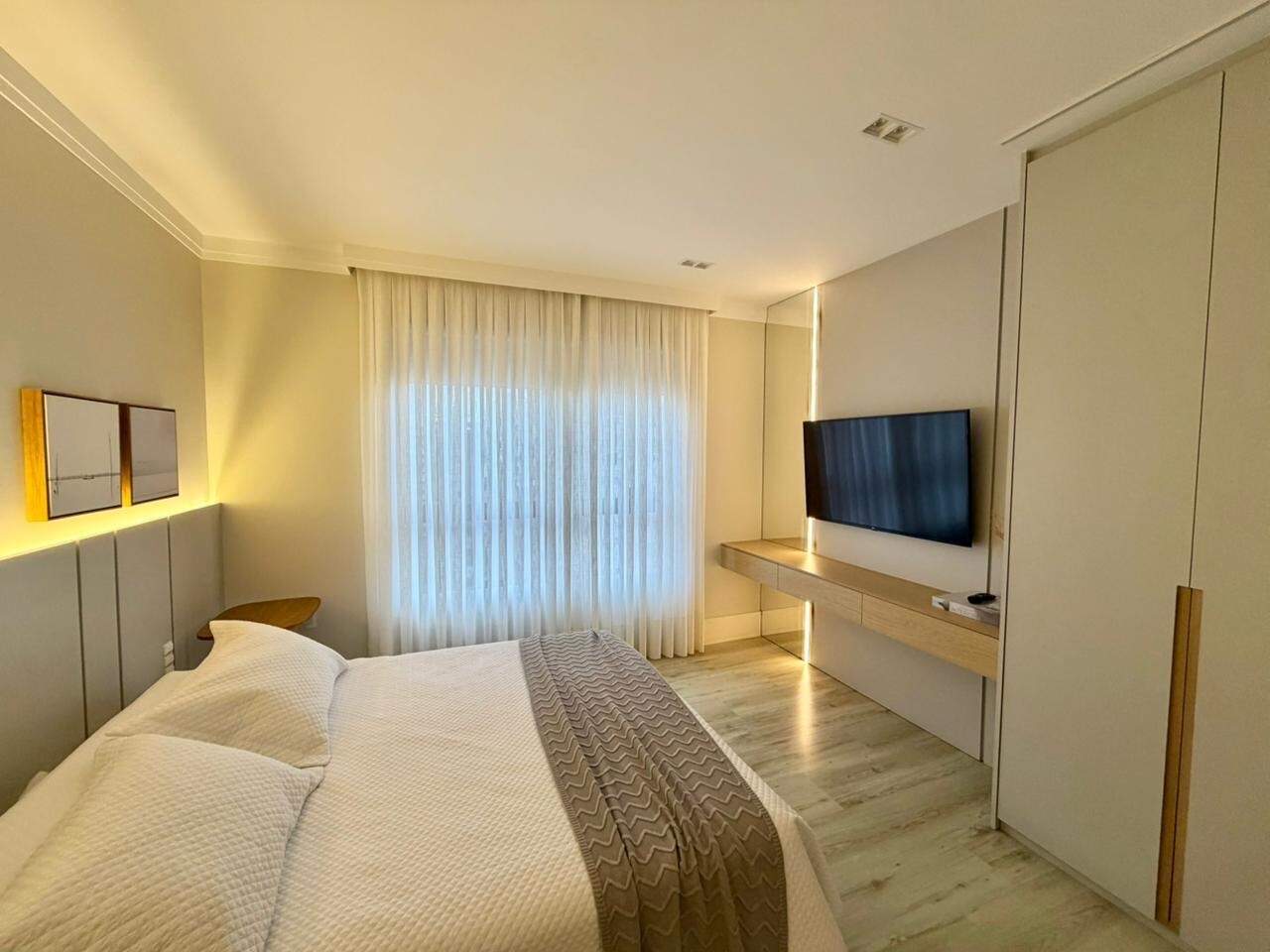 Suíte com painel de TV e bancada, em apartamento decorado