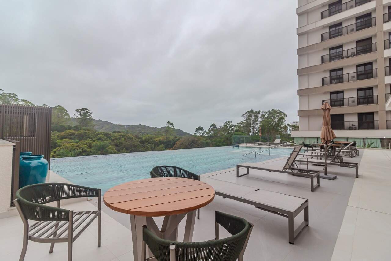 Deck da piscina com mesas e a mata ao fundo
