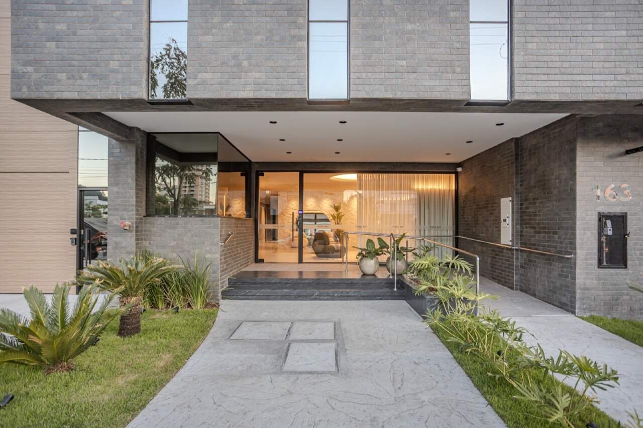 Entrada do prédio com jardim, rampa e portaria envidraçada