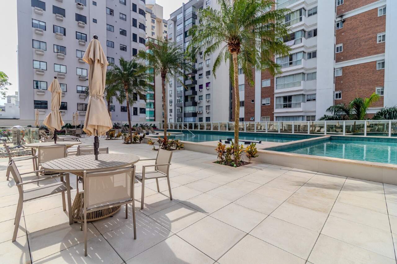 Deck do lazer com mesas, guarda-sóis e a piscina ao fundo
