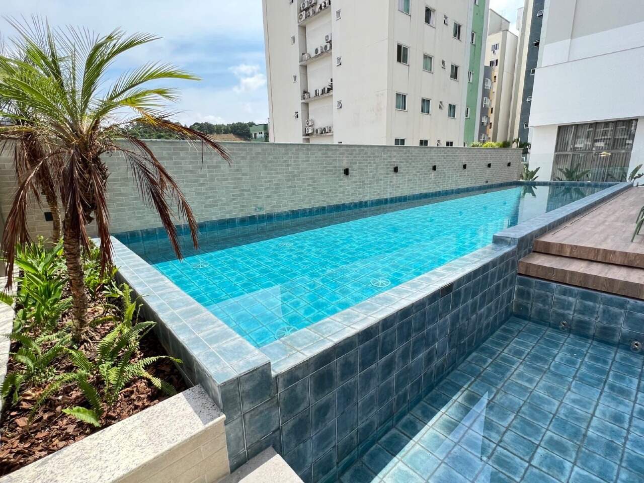 Piscina com borda revestida e jardim tropical
