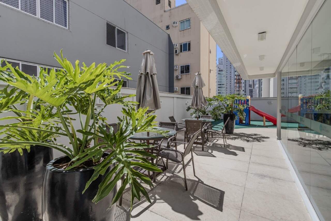 Terraço coberto com mesas e ombrelones, com o playground ao fundo