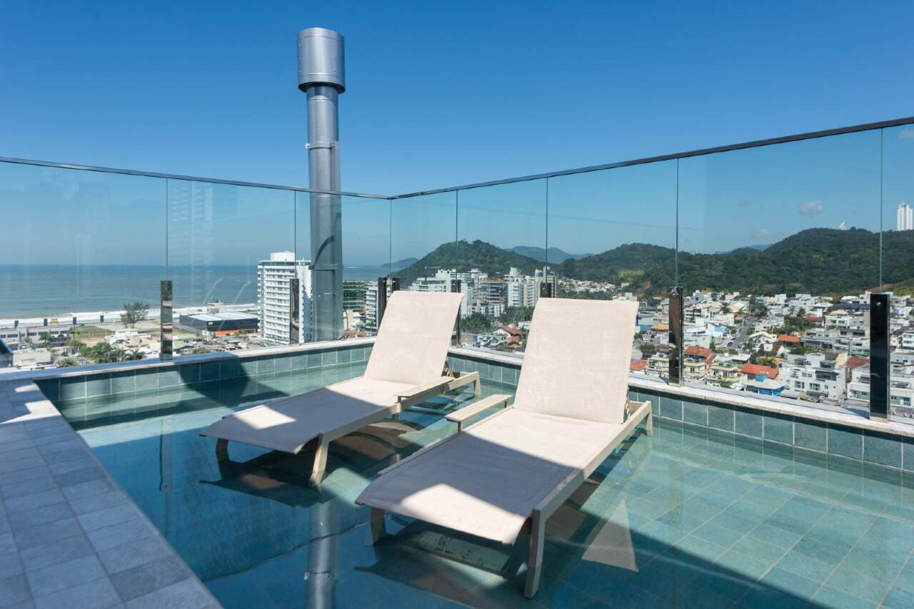 Piscina do rooftop com espreguiçadeiras no deck molhado e o mar ao longe