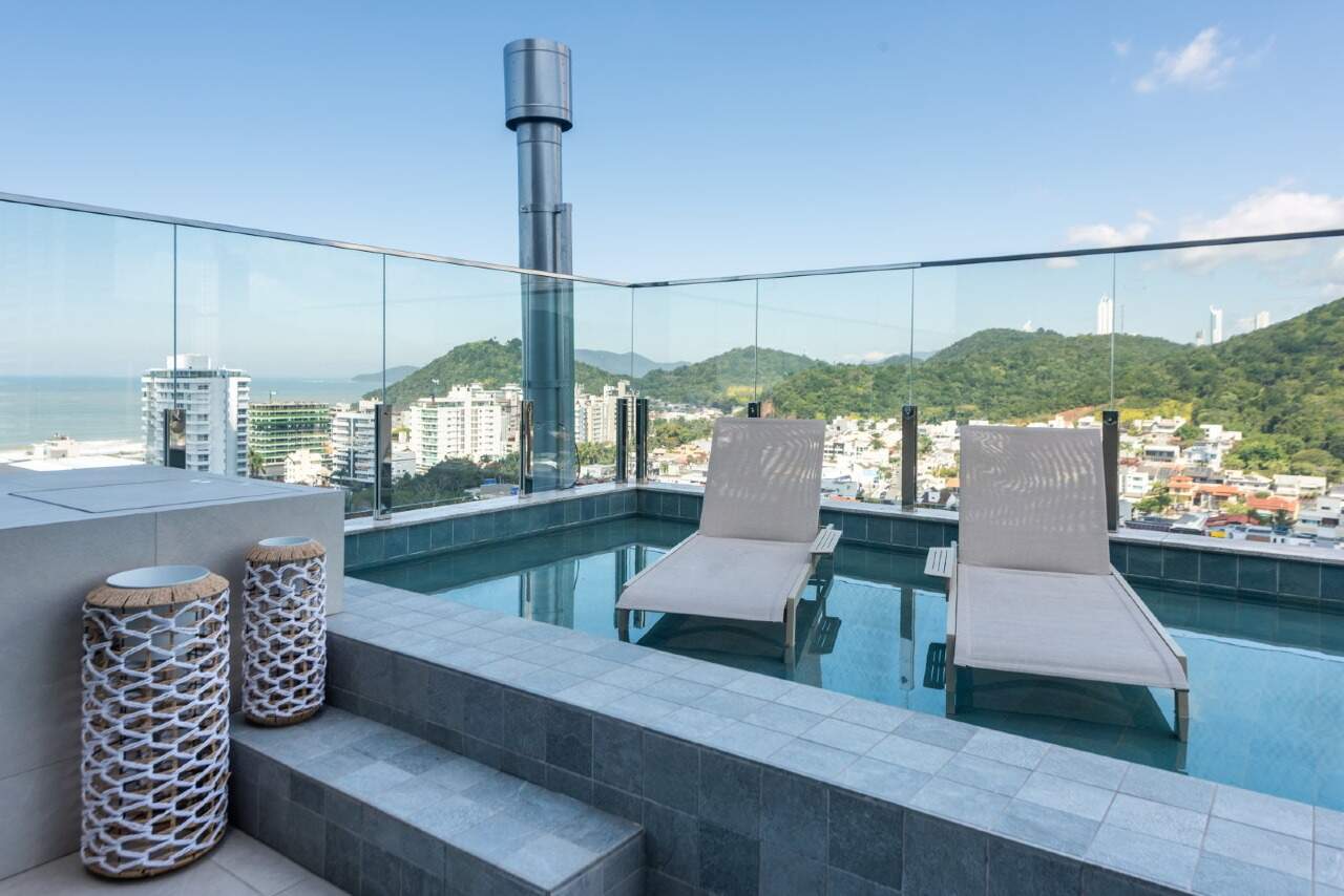 Piscina do rooftop com deck molhado, o mar à esquerda e os morros ao fundo