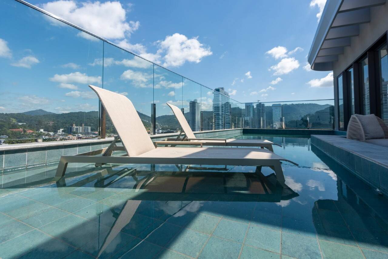 Espreguiçadeiras dentro da piscina do rooftop, com guarda-corpo de vidro