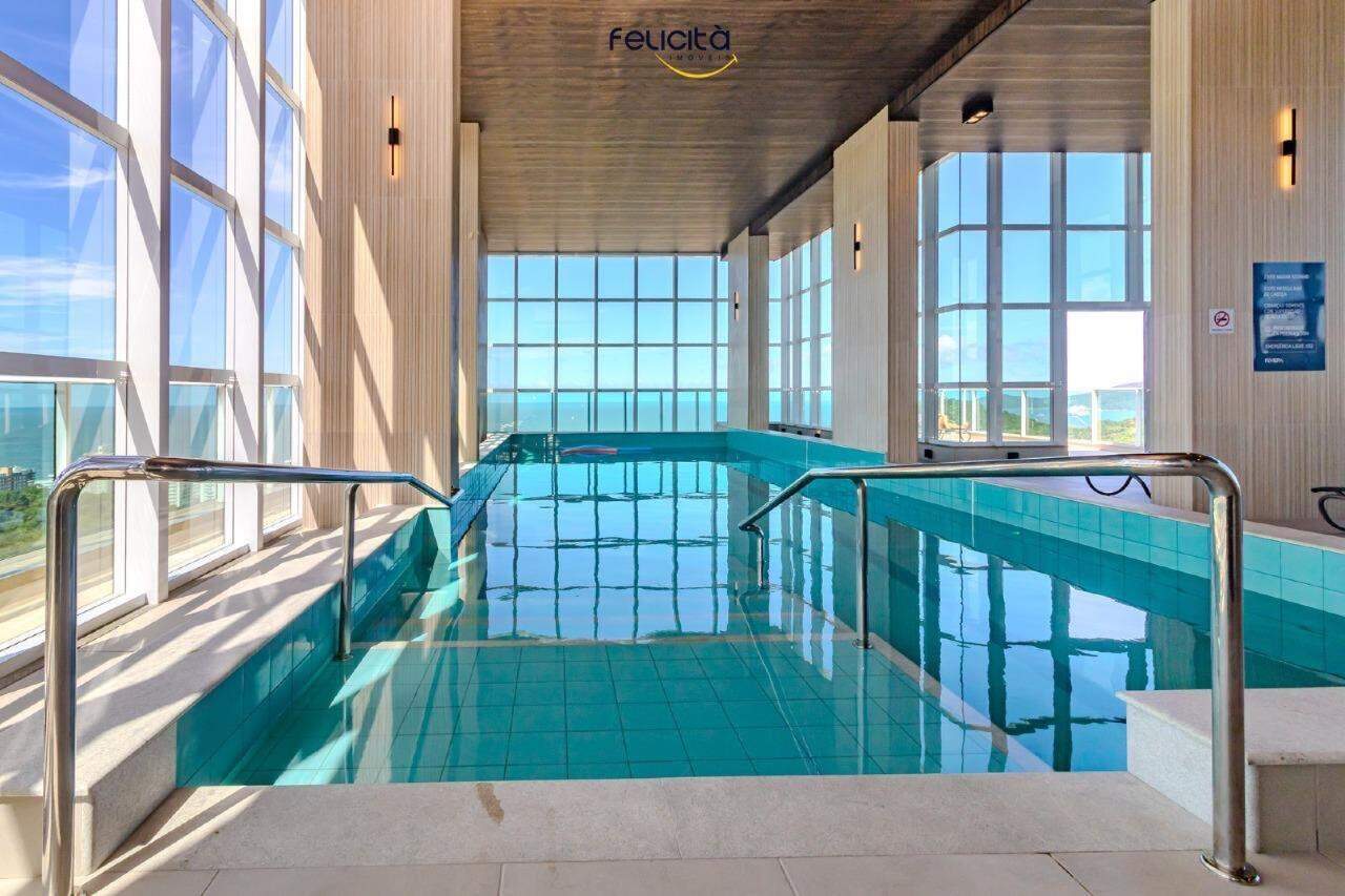 Piscina coberta com raias e o mar ao fundo, pelas janelas de vidro