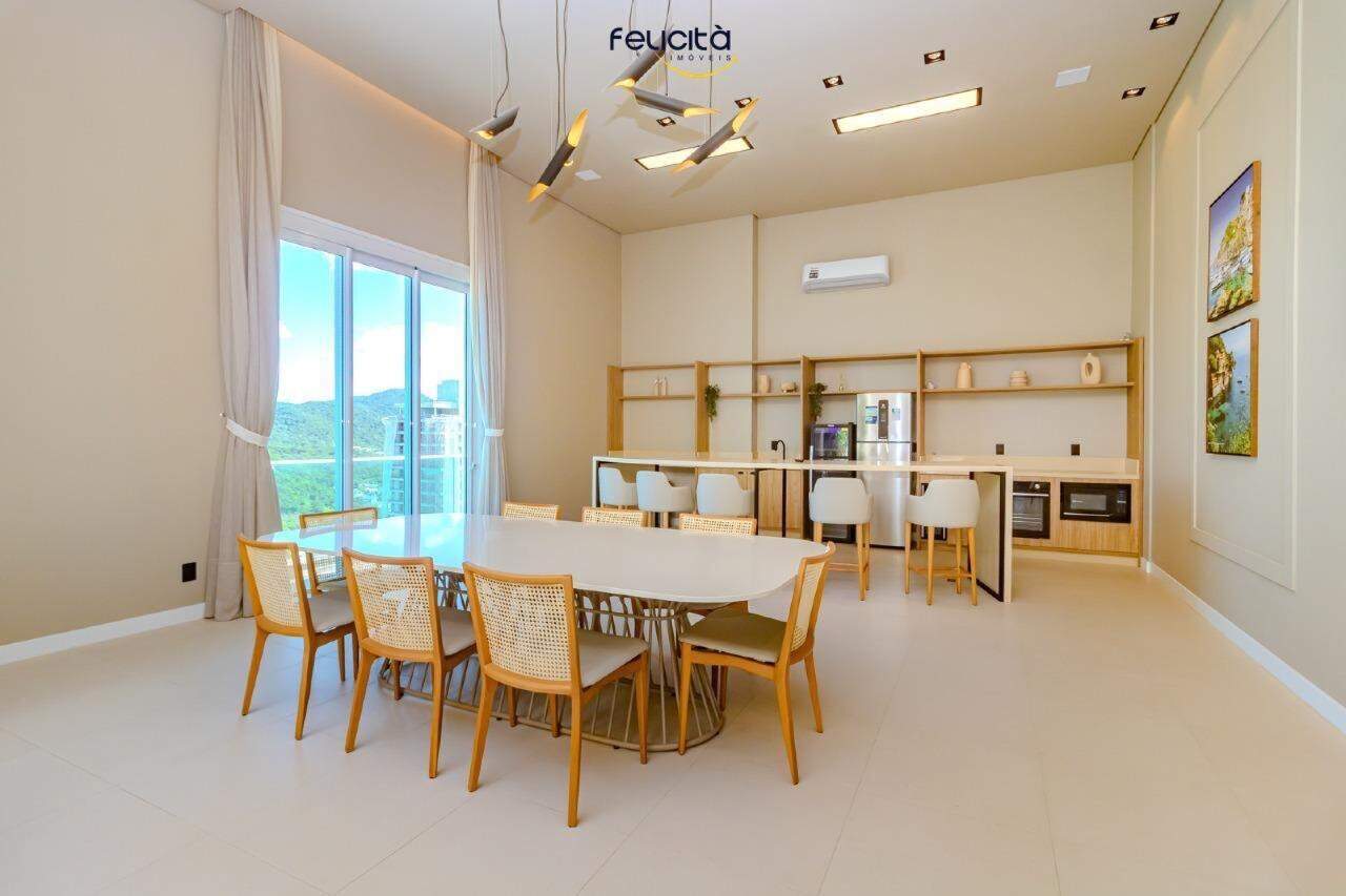 Salão com mesa oval, cozinha e janelas para a Praia Brava