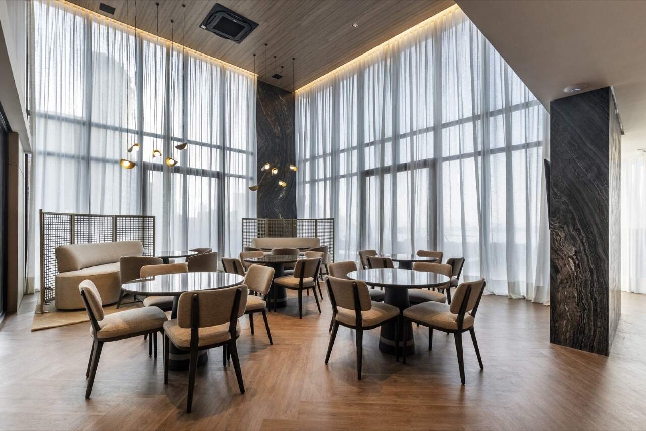 Espaço gourmet com mesas redondas e cortinas do piso ao teto