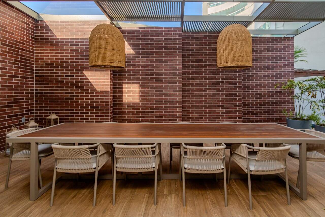 Área externa com mesa comunitária, luminárias de palha e parede de tijolos