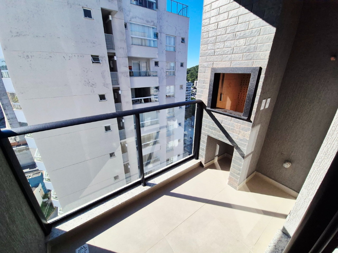 Apartamento à venda no Praia Brava: Sacada com guarda-corpo de vidro e churrasqueira, com prédios vizinhos em frente