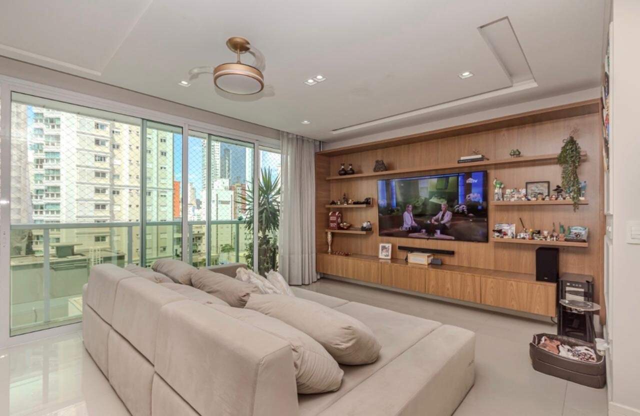 Apartamento à venda no Centro: Living com sofá amplo, painel de madeira para TV e portas de vidro para a sacada