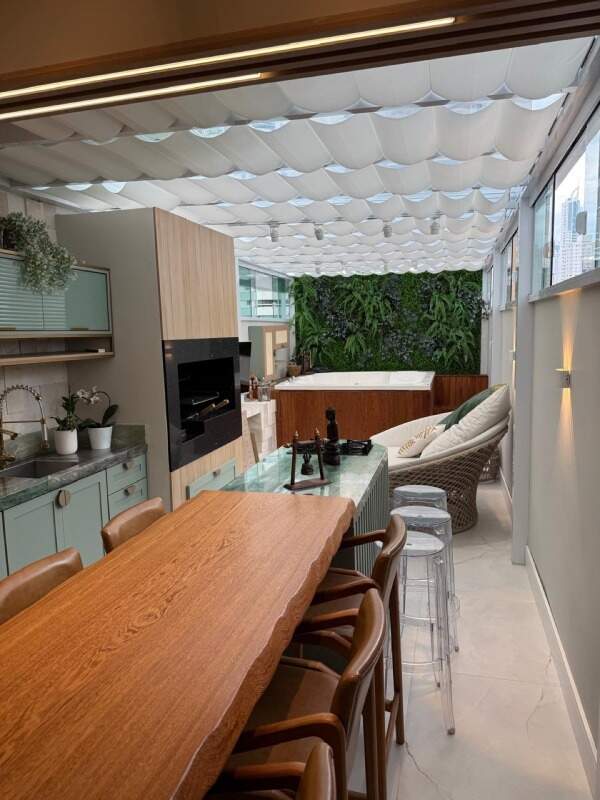 Apartamento à venda no Centro: Área gourmet envidraçada com mesa de madeira, churrasqueira e spa ao fundo