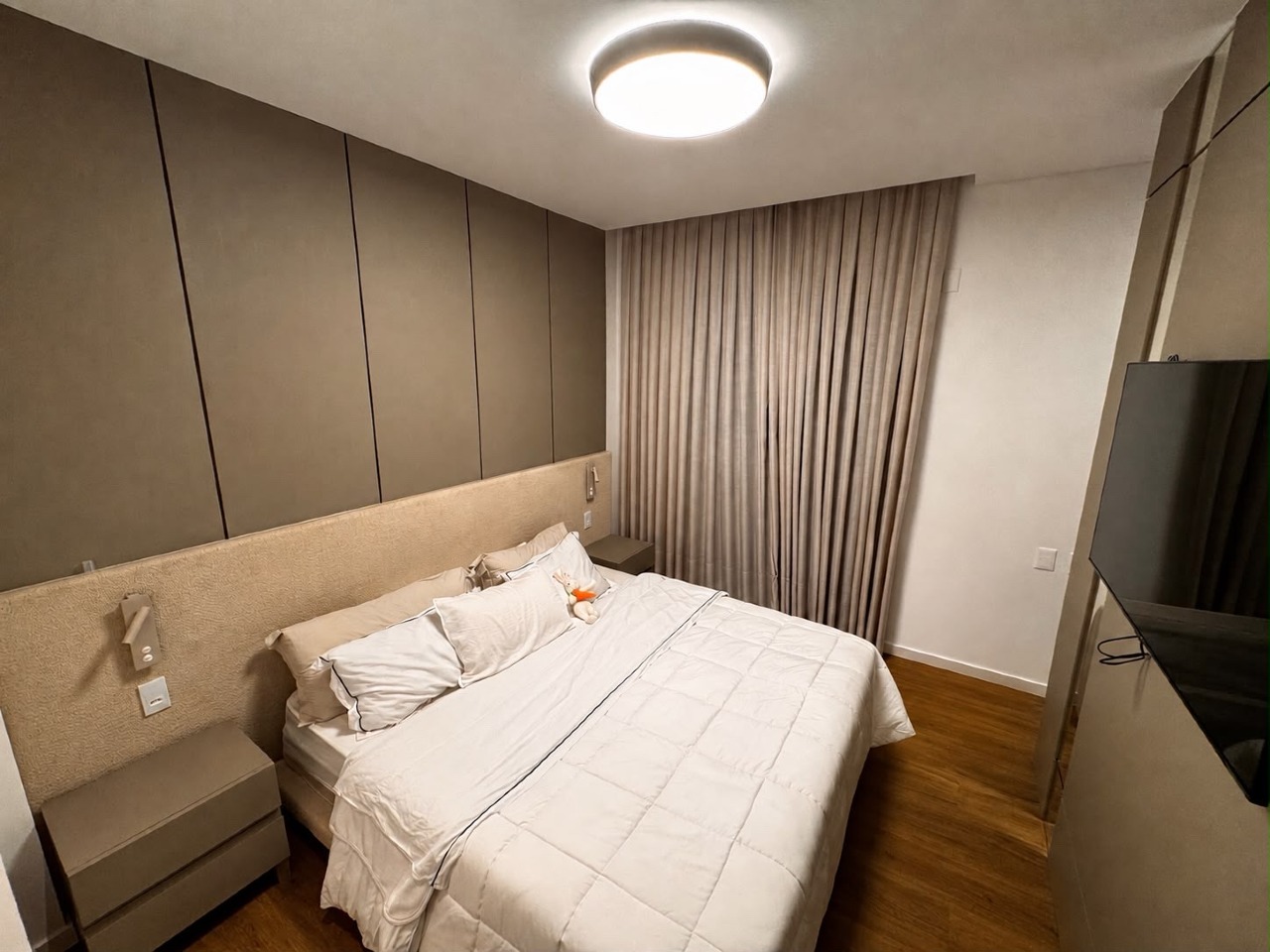 Apartamento à venda no Centro: Suíte com painéis em tom cinza, cabeceira estofada e cortina blecaute