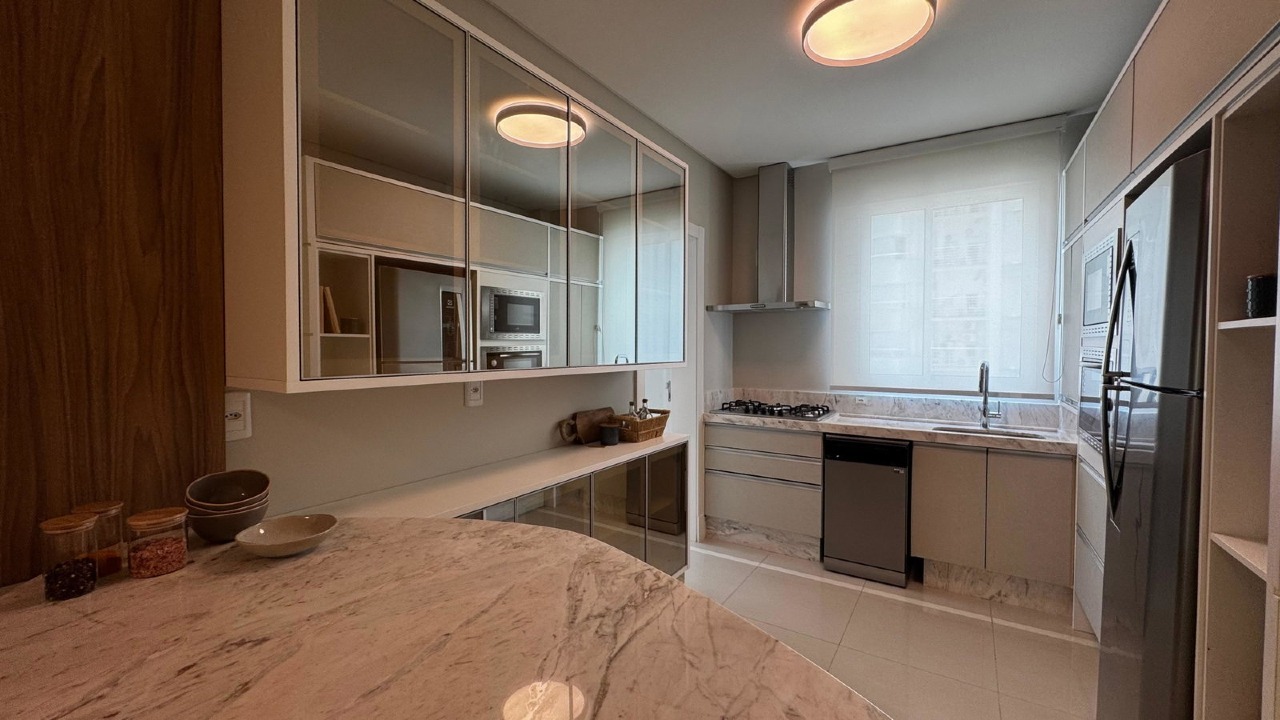 Apartamento à venda no Centro: Cozinha planejada com cooktop, coifa, fornos embutidos e bancada curva de pedra