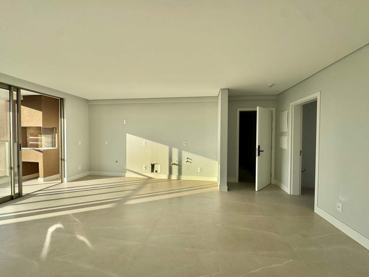 Apartamento à venda no Centro: Living com porcelanato, a sacada à esquerda e a parede da cozinha com pontos de água e luz