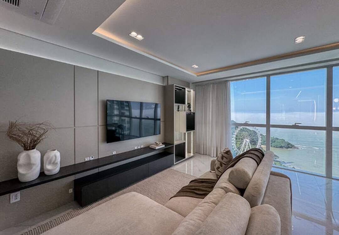 Apartamento à venda no Pioneiros: Living com sofá e janelas do piso ao teto para a roda-gigante e o mar, no Skyline Tower