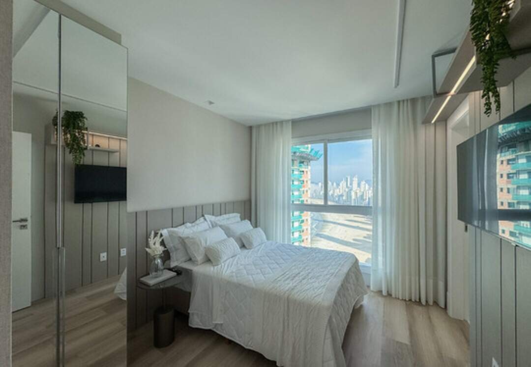 Apartamento à venda no Pioneiros: Suíte com cabeceira em painel, TV e janela voltada para a praia