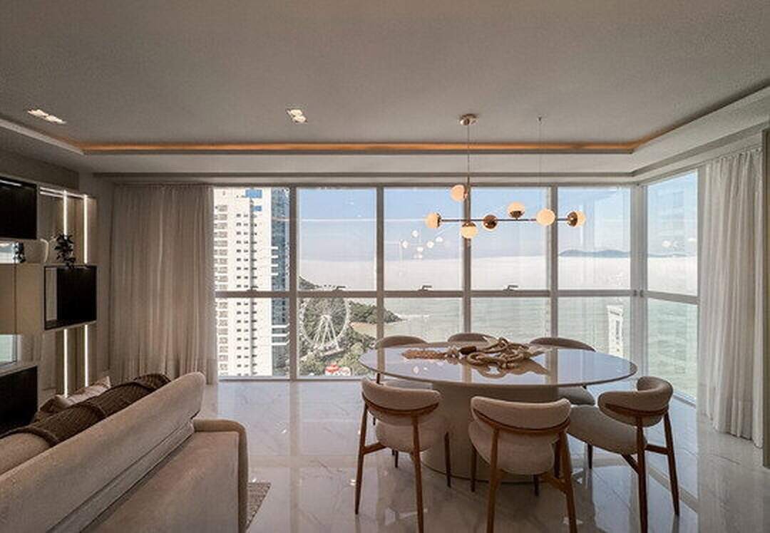 Apartamento à venda no Pioneiros: Mesa de jantar oval diante das janelas, com a roda-gigante e o mar ao fundo