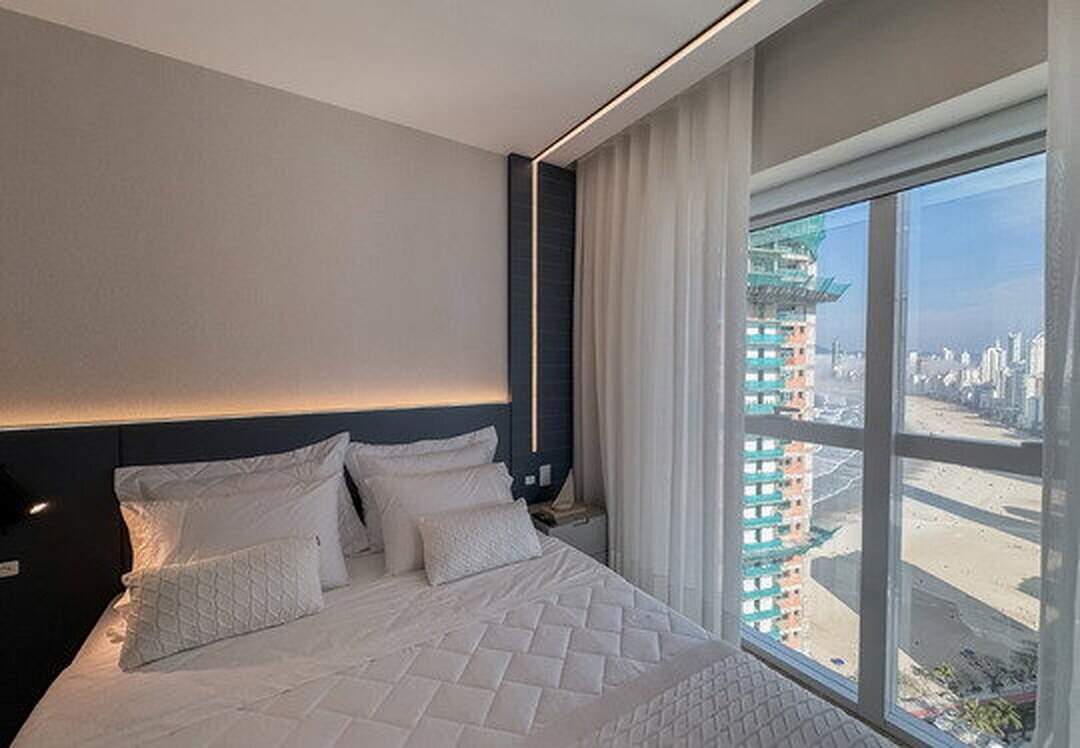 Apartamento à venda no Pioneiros: Suíte com cabeceira azul e janela para a praia e a cidade