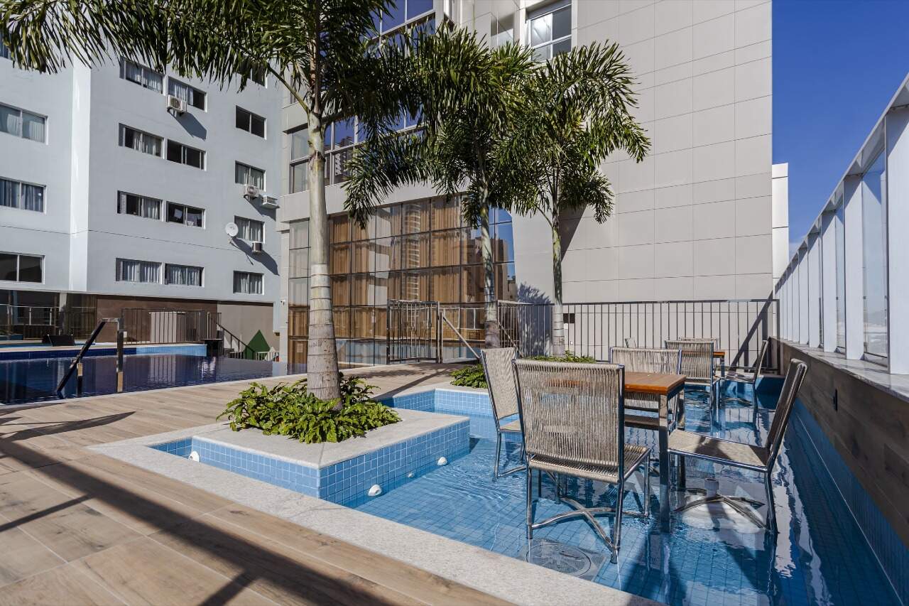 Apartamento à venda no Centro: Mesa e cadeiras na lâmina d’água da piscina, entre palmeiras