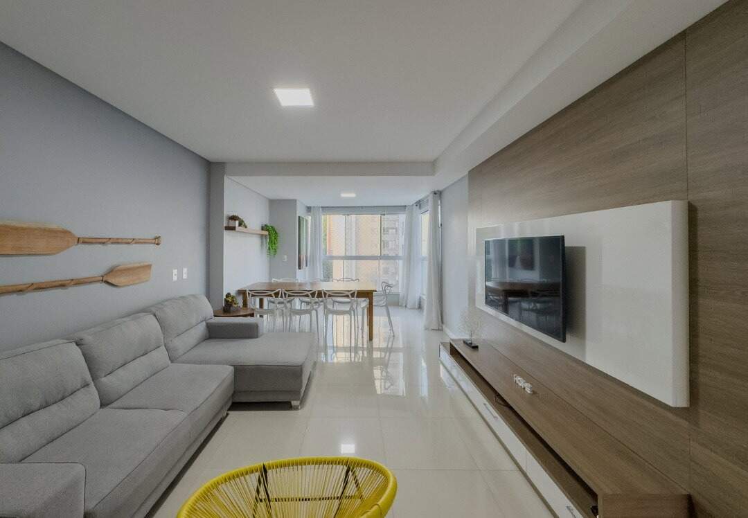 Apartamento à venda no Pioneiros: Living com sofá e painel de TV em madeira, piso em porcelanato