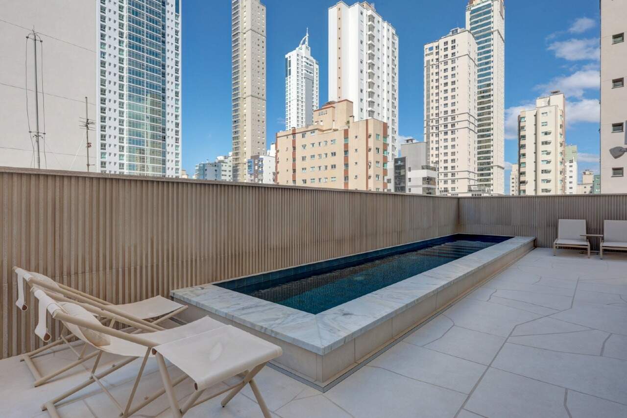 Apartamento à venda no Centro: Deck da piscina com espreguiçadeiras, cercado pelas torres do Centro