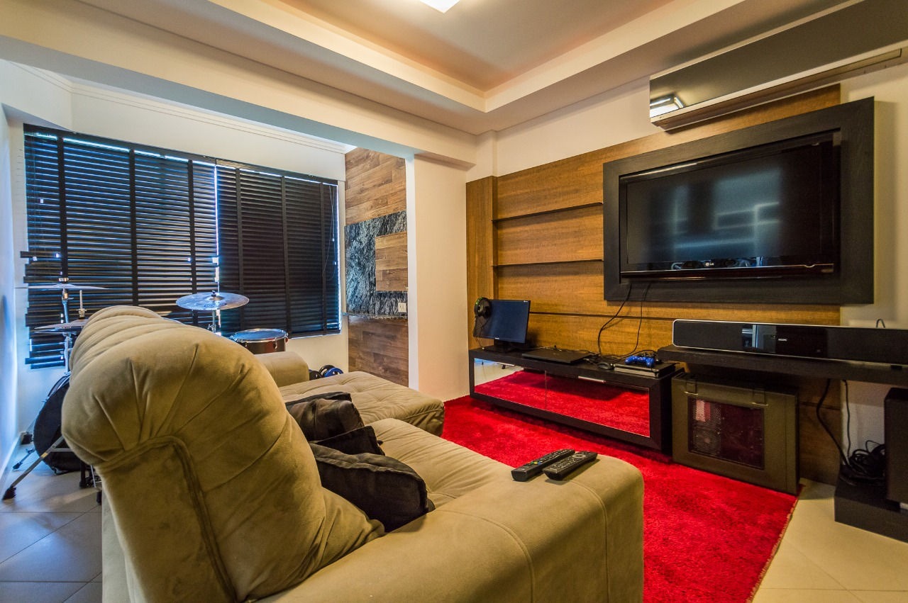 Apartamento à venda no Fazenda: Estar com sofá, tapete e painel de TV em madeira