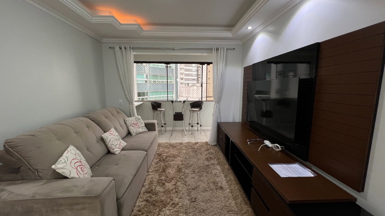 Apartamento à venda no Centro: Living com sofá, painel de TV e sanca iluminada, com a sacada ao fundo